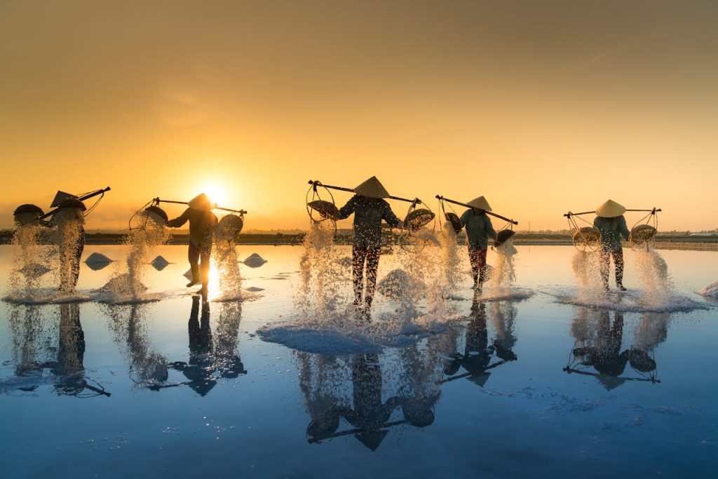pexels-photo-2132048 Fishermen collecting salt at sunset, reflecting in water, showcasing traditional methods.